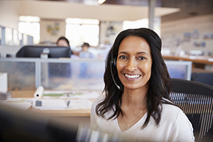 Woman with headset in front of computer looking at the camera